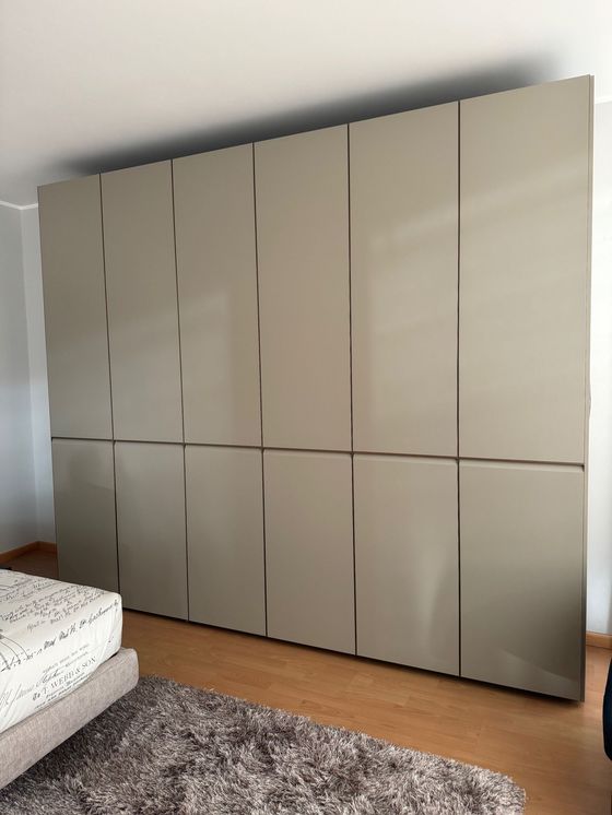 Ampio armadio beige con linee verticali scure. Camera da letto con letto e tappeto.