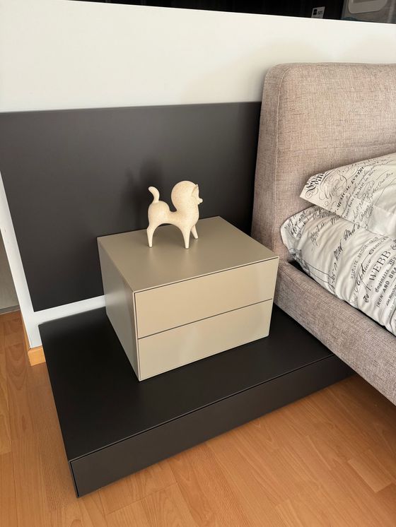 Comodino beige con statuetta di cane accanto al letto, contro una parete grigio scuro.