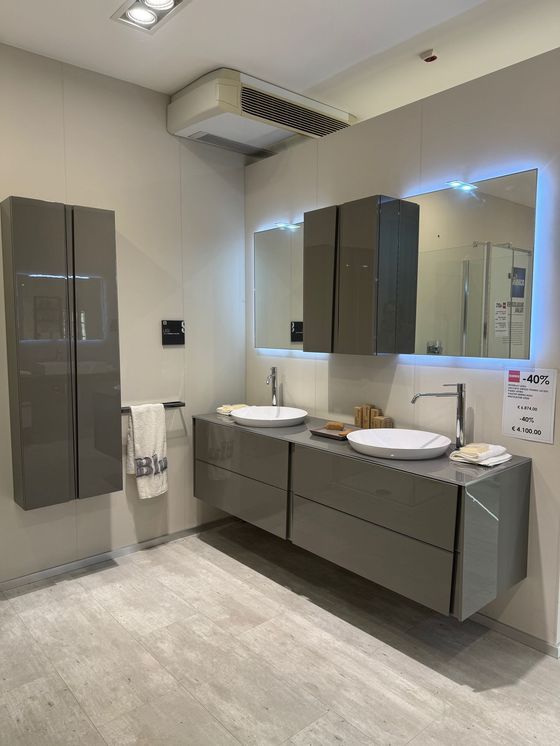 Moderno bagno grigio con mobile lavabo sospeso, armadietti e specchio con luci a LED.