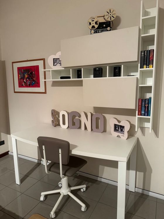 Scrivania bianca con ripiani annessi, sedia grigia, quadro incorniciato e lettere decorative con la scritta 