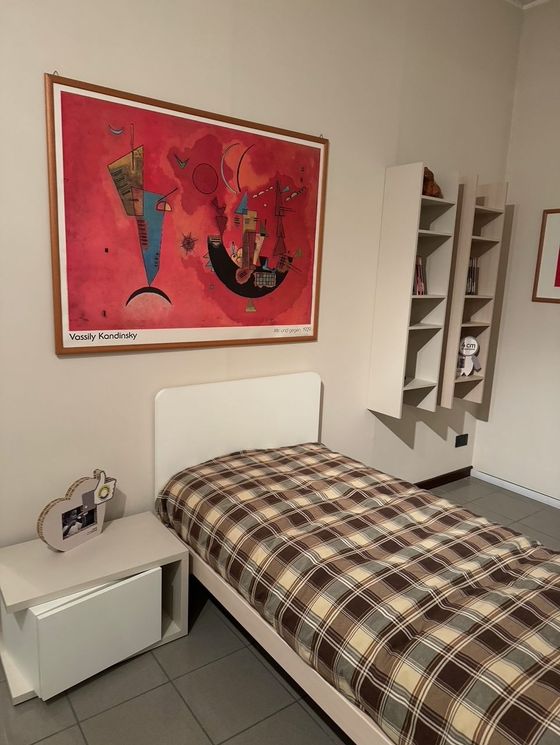 Camera da letto con letto singolo, comodino e quadro astratto. Colori rosso, marrone e bianco.