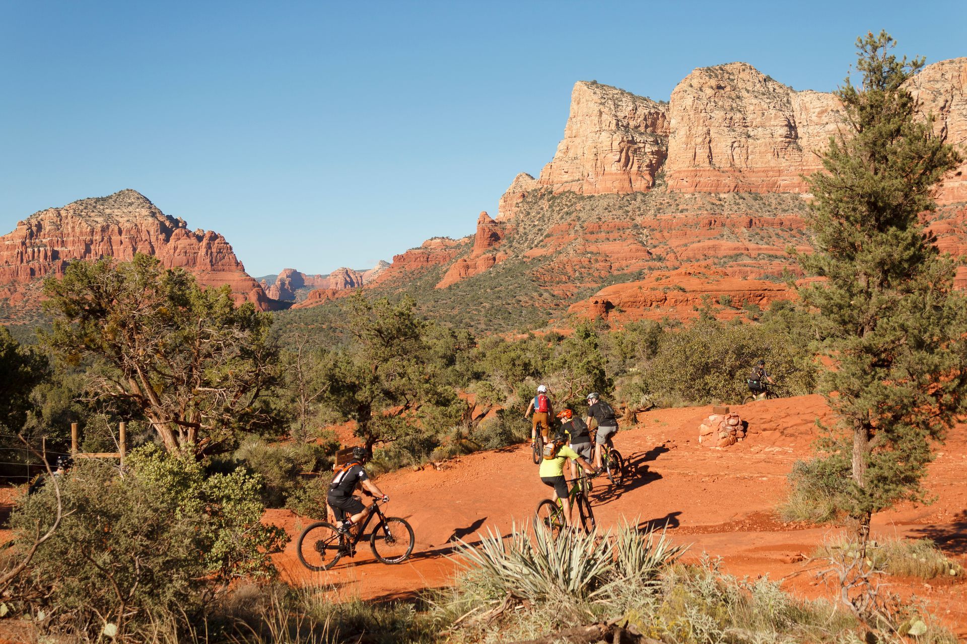 Mountain bikers on a red dirt trail in Sedona, Arizona, with red rock formations in the background.