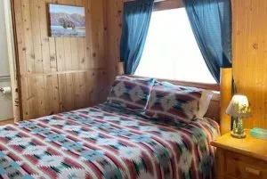 A bedroom with a bed , nightstand , lamp and window.
