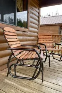A wooden rocking chair is sitting on a wooden deck in front of a log cabin.