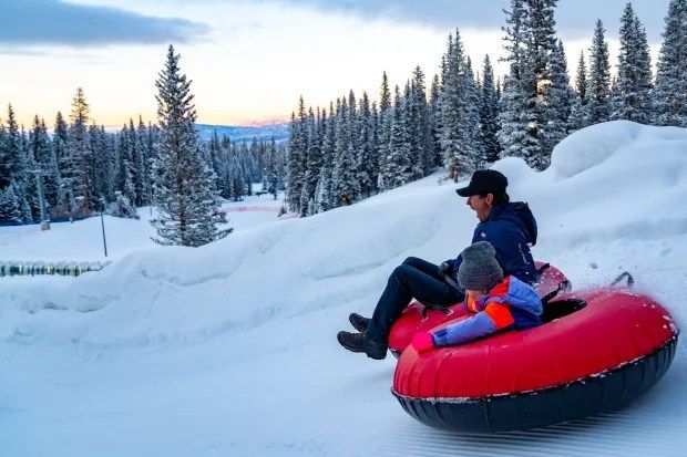 A man and a child are riding down a snow covered hill on a tube.