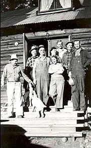 A group of people are standing on the steps of a log cabin.