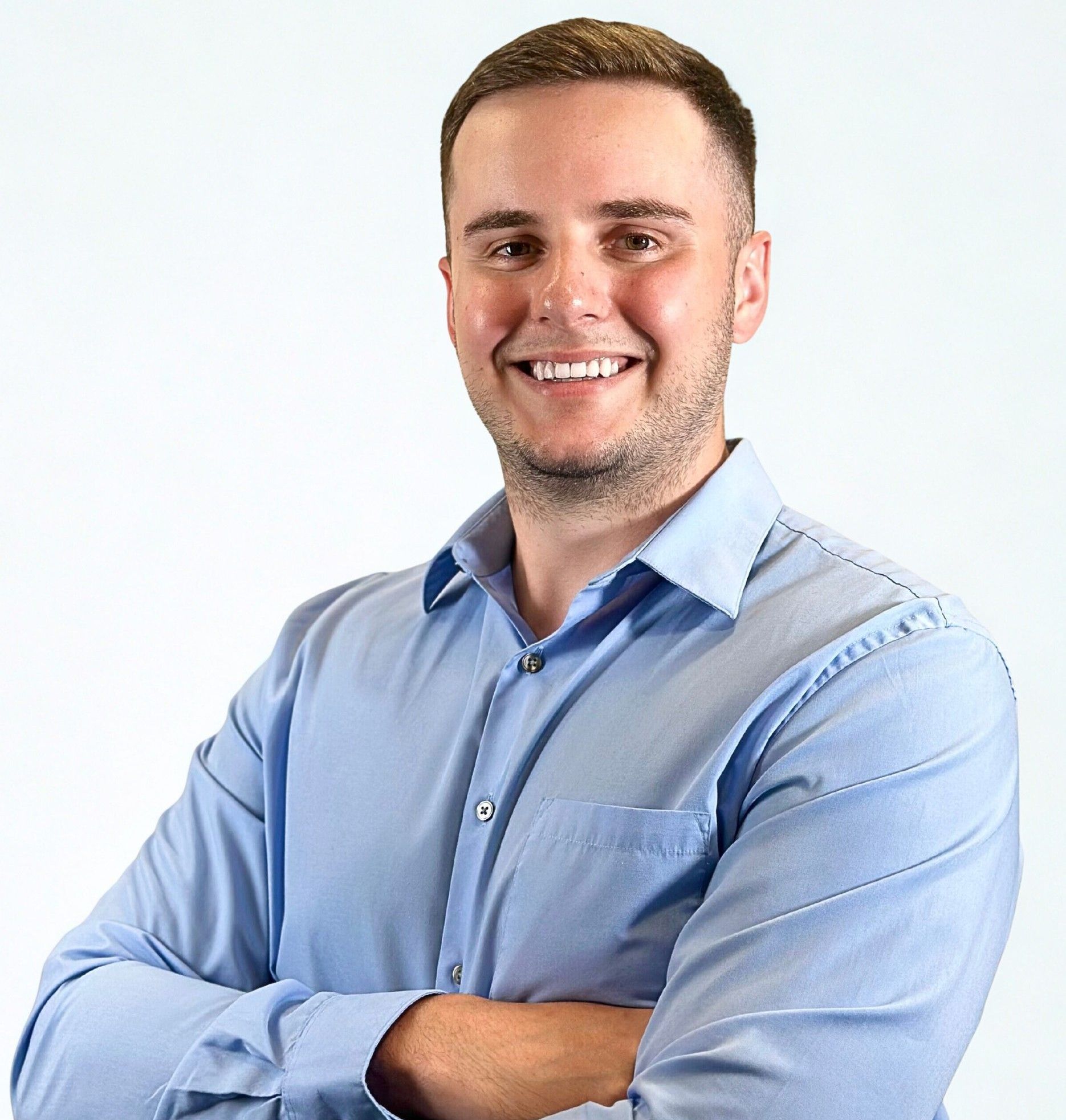A man in a blue shirt is smiling with his arms crossed