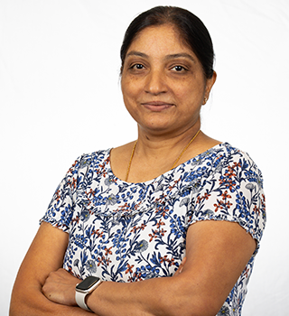 A woman wearing a watch and a floral shirt is standing with her arms crossed.