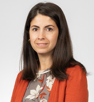 A woman wearing an orange sweater and a floral shirt is smiling for the camera.