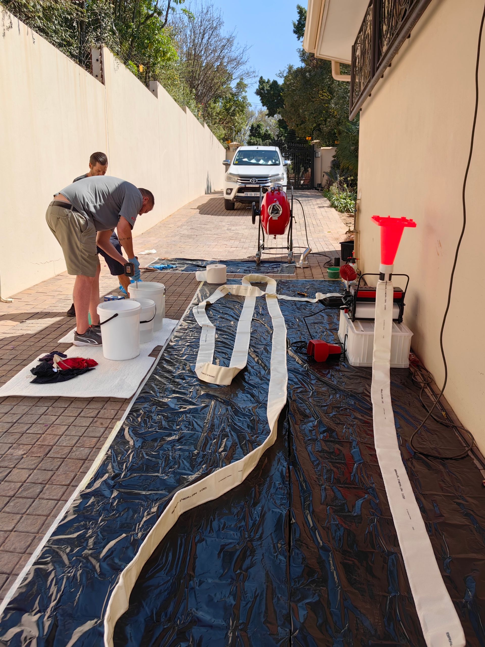 Two men are working on relining a pipe outside of a building.