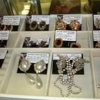A retail display tray containing several pairs of vintage-style costume earrings and clip-on jewelry with price tags.