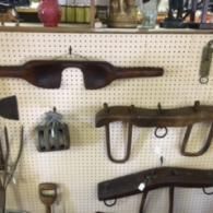 Wooden farming yokes and vintage metal tools hang on a white pegboard display wall.