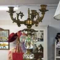 An ornate, antique brass candelabra lamp with crystal accents sits in a shop against a pegboard background.