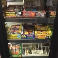 A glass display case filled with vintage collectible boxes and action figure sets on three shelves.