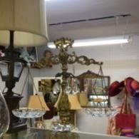 An ornate, golden antique tabletop scale with crystal hanging bowls sits on a glass surface in a vintage shop.