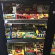 A display cabinet shelf filled with assorted boxes of retro trading cards and collectibles.