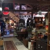 An interior view of a rustic antique shop filled with wooden furniture, decor, and items under exposed wooden rafters.