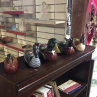 A row of five decorative ceramic duck figurines lined up on a dark wood shelf in a store.