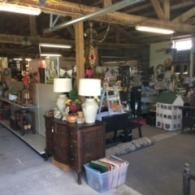An interior view of a rustic, wood-beamed antique shop filled with assorted furniture, lamps, and collectibles.