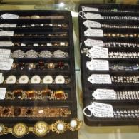 Two velvet trays filled with various bracelets and jewelry pieces, each tagged with price labels in a display case.