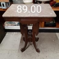 A small wooden pedestal table with a rectangular marble top, marked with a price of 89.00, sitting on a concrete floor.