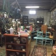 An antique shop interior featuring a wooden display counter, various decorative items, and two light blue chairs.