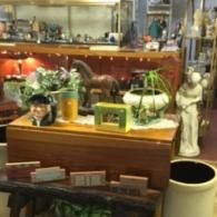 A wooden drop-leaf table displaying a horse figurine, a green box, and various decor items inside a cluttered antique shop.