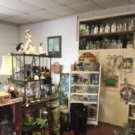 A cluttered shop interior with a tiered metal shelf displaying figurines, a framed picture, and a wooden storage unit.