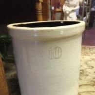 A large, white stoneware crock featuring a prominent hand-drawn number 10 on its front, sitting in an indoor setting.