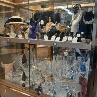 A display case filled with crystal glassware, decorative figurines, and jewelry on shelves.