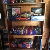 A wooden shelf displays three levels of collectible model cars in their original packaging.