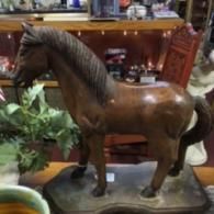 A carved wooden horse figurine with a dark finish standing on a decorative base in a shop.