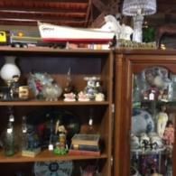Two wooden shelves filled with antiques, including a model boat, lamps, books, and various glass and ceramic items.