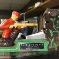 A vintage cast-iron shooting gallery toy with a figure aiming a rifle at a tree trunk, labeled 