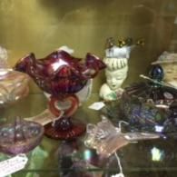 A shelf filled with vintage glassware, including a red ruffled bowl, a decorative head vase, and a glass butterfly.