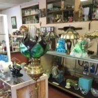 Antique shop interior featuring a green and black tulip-style lamp on a stand, with shelves of glass decor and lamps.