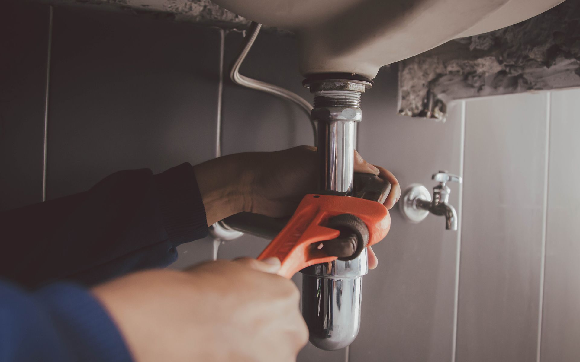 A person using a wrench to work on plumbing under a sink in a bathroom.