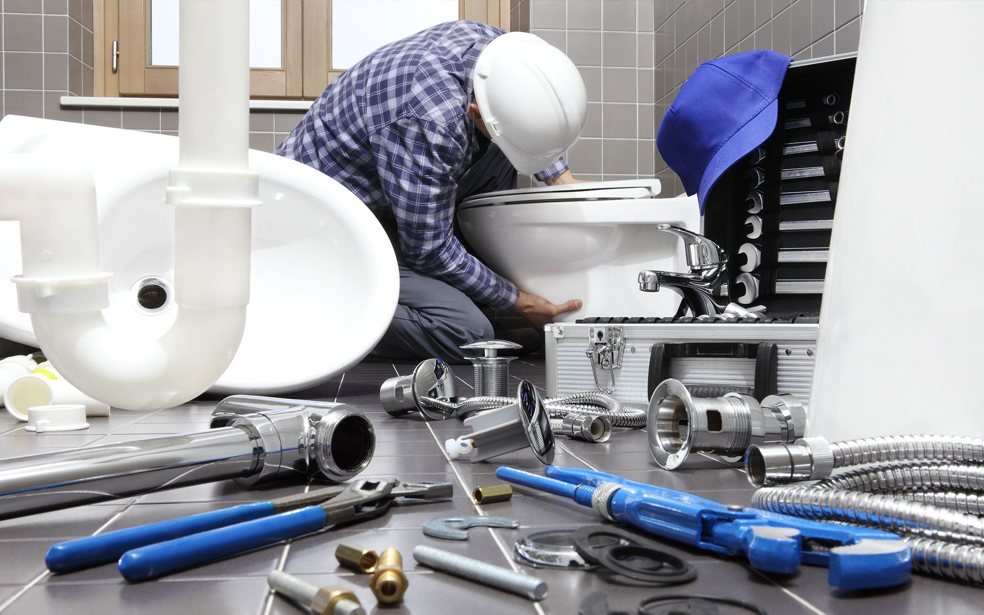 Plumber installing a toilet, surrounded by tools and plumbing parts in a bathroom.