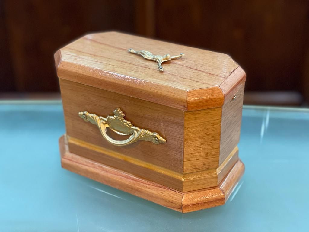 Una pequeña caja de madera con un asa dorada reposa sobre una mesa de cristal.