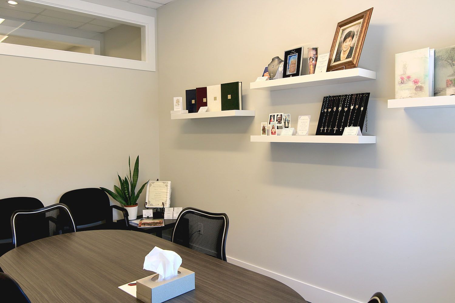 A conference room with an oval table, chairs, a small plant, and three white shelves displaying framed photos and items.