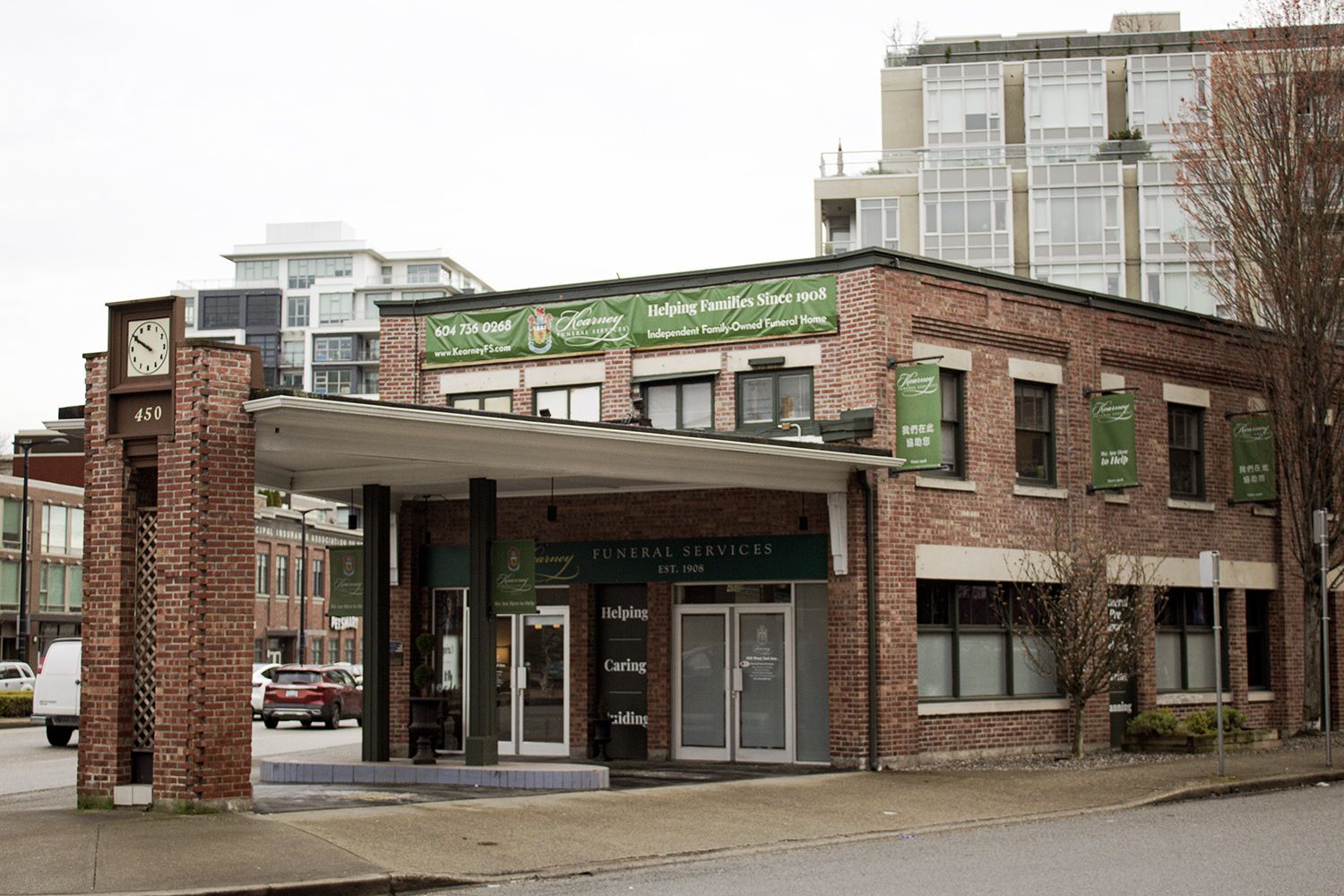 A red brick building with a drive-through canopy and a tall clock tower, situated on a street corner.