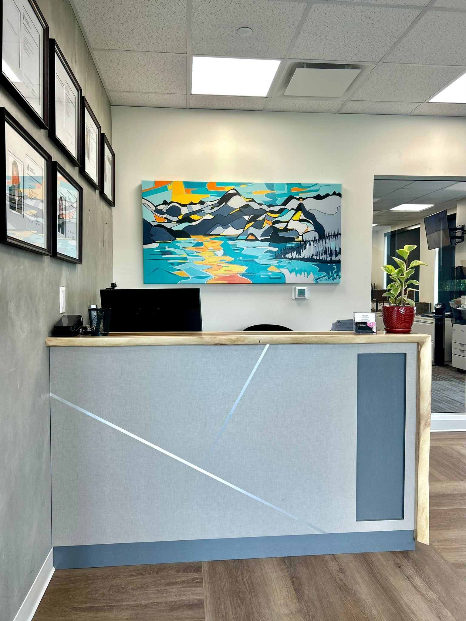 A reception desk in a modern office with a colorful abstract mountain painting on the wall above and framed art on the left.