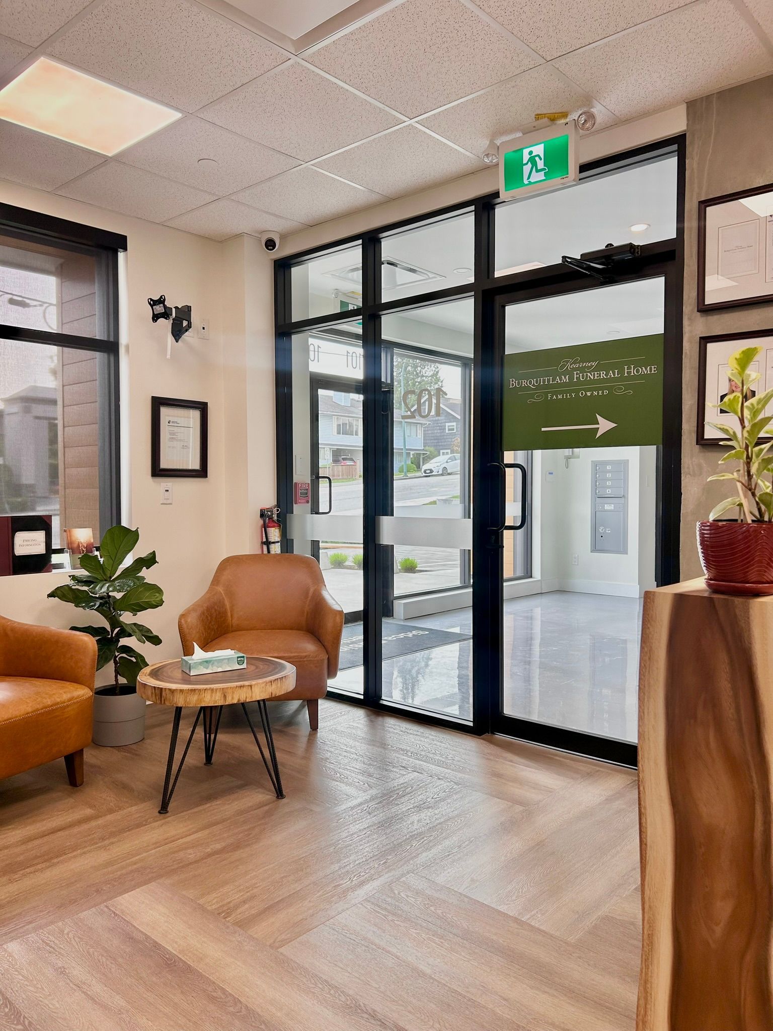 A reception waiting area featuring leather armchairs, a wooden coffee table, a potted plant, and a glass-paneled entry door.