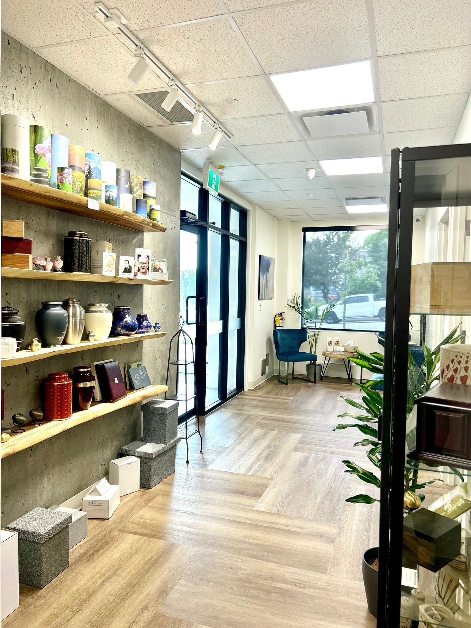 A retail space with shelves lining a concrete wall displaying various canisters and urns, leading to an office area.