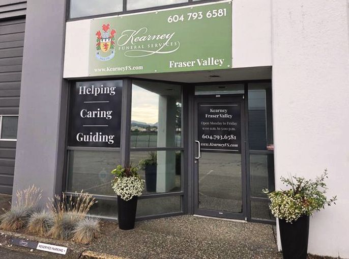 Exterior view of Kearney Funeral Services office with green signage, glass door, and black planters at the entrance.