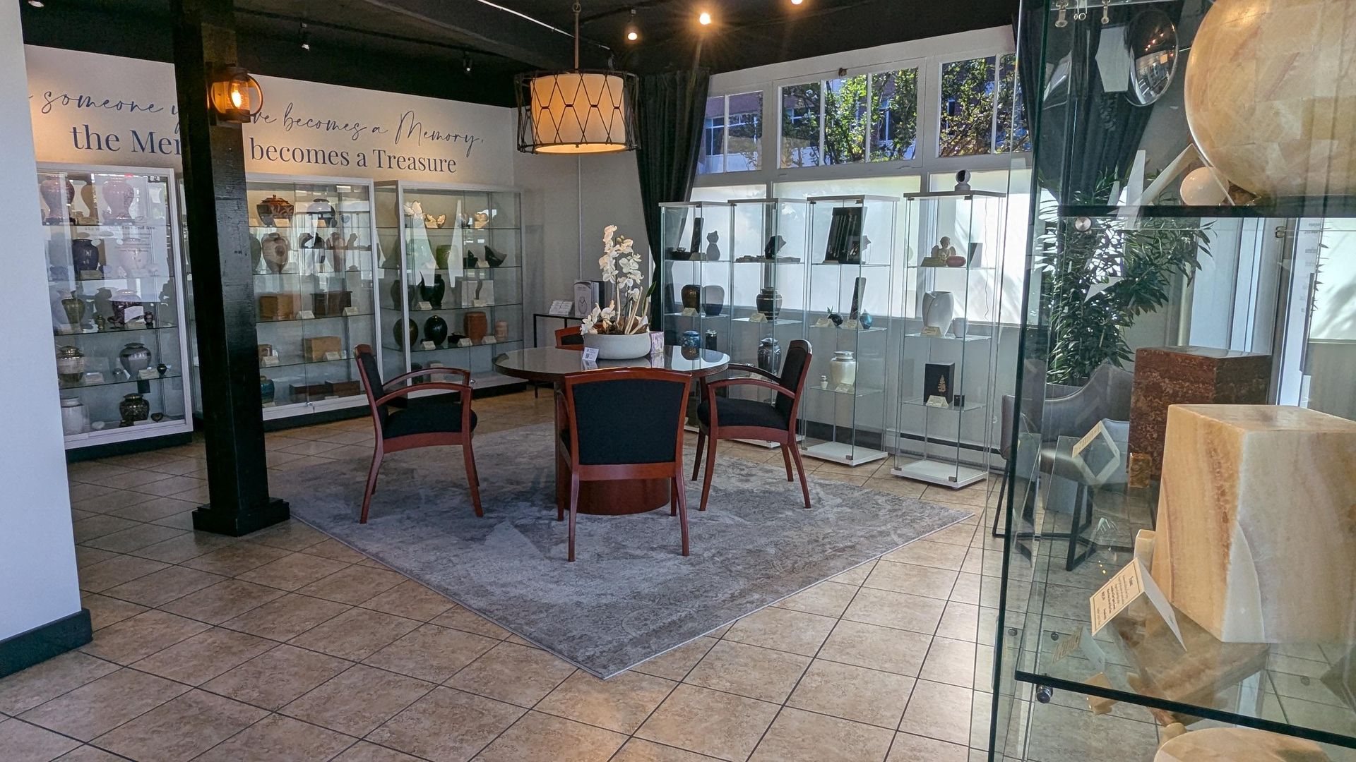 A bright room with display cases filled with items, a central table with two chairs, and a patterned rug on tiled floors.