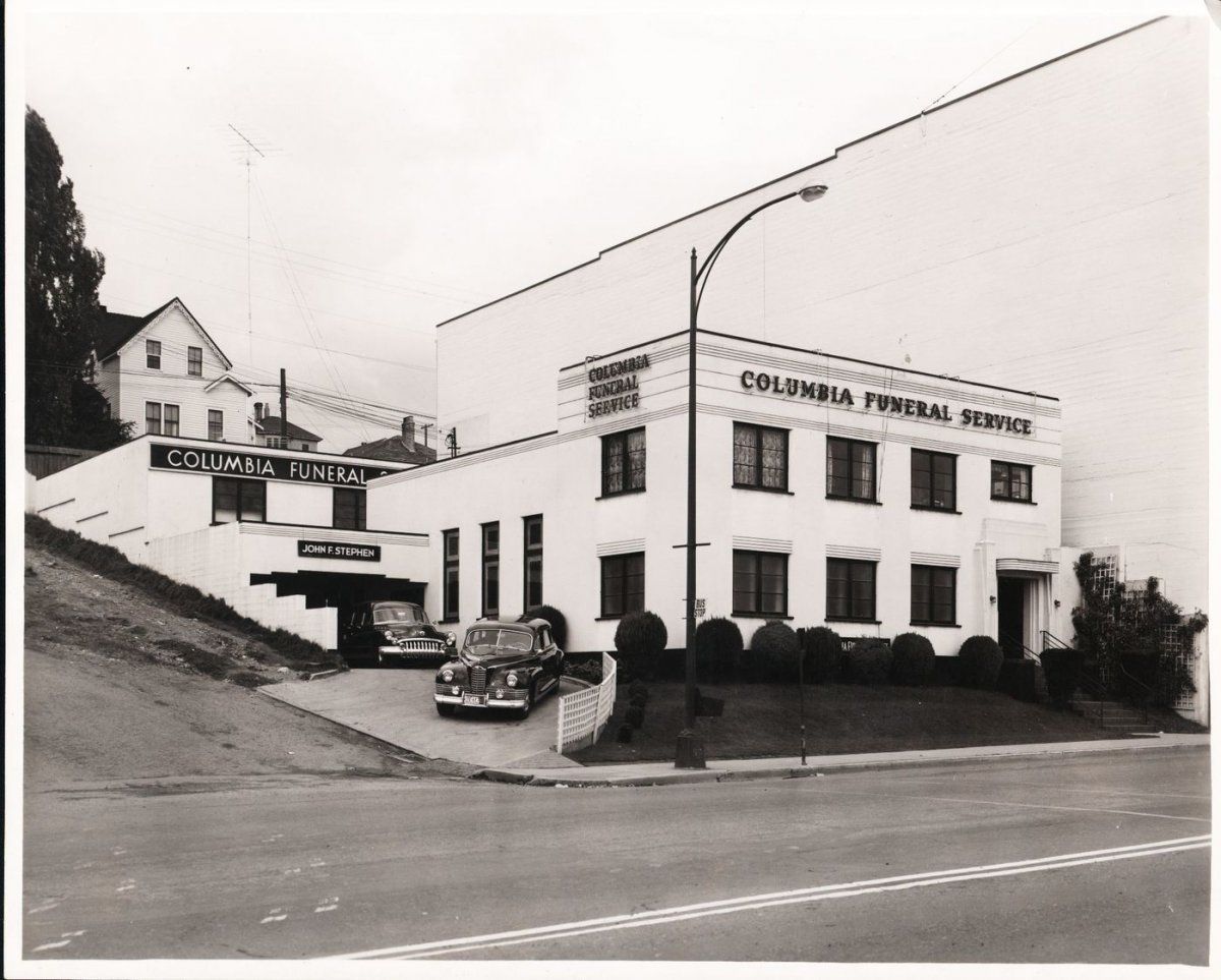A black-and-white vintage photo of the Columbia Memorial Service funeral home building with cars parked in the driveway.