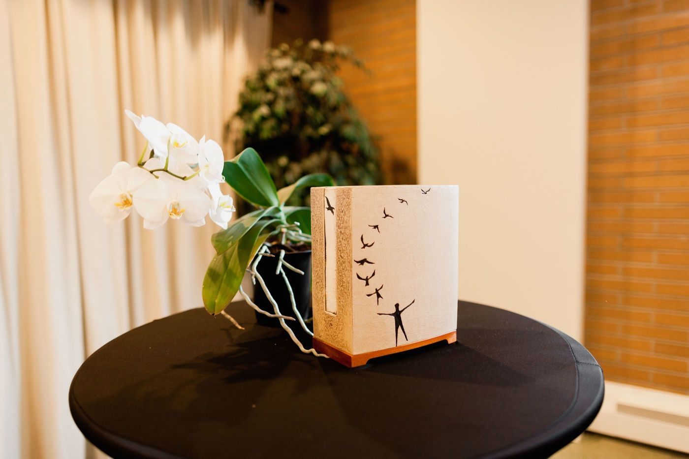 An orchid and a commemorative urn with a figure and birds illustration sit on a black table.