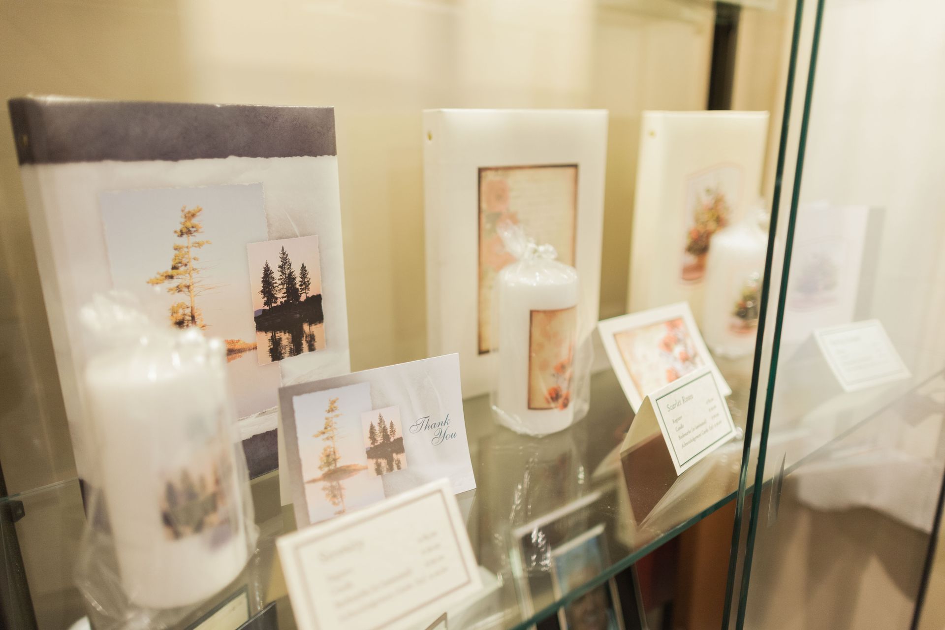 Artistic candles and printed displays with nature imagery are arranged on glass shelves inside a store display case.