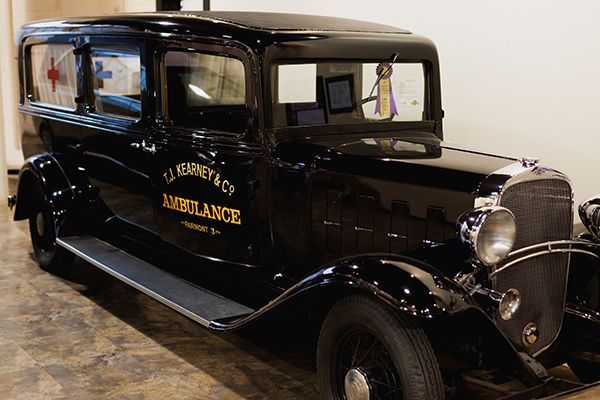 A black vintage T.J. Kearney & Co. ambulance parked indoors, featuring gold lettering on the side door.